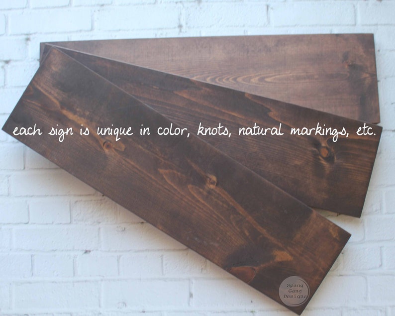 May include: Three wooden signs stacked on top of each other. The signs are a dark brown color and have a natural wood grain. The text "each sign is unique in color, knots, natural markings, etc." is written in white on the top sign. The text "Spang Gang Desiang" is written in white on the bottom sign.