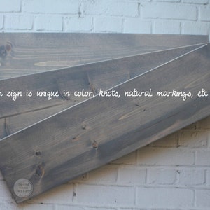 May include: Three pieces of wood, stacked on top of each other, with a gray stain. The wood has a natural grain and knots. The text "each sign is unique in color, knots, natural markings, etc." is written on the wood. The text "Spang Gang Designs" is written on a small circle in the bottom right corner.