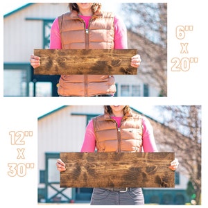 May include: Two wooden signs, one 6 inches by 20 inches and the other 12 inches by 30 inches, are held by a person in front of a barn. The signs are stained a dark brown color.