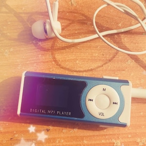 Peut inclure: Un lecteur MP3 numérique rectangulaire bleu et blanc avec un écran noir affichant le texte DIGITAL MP3 PLAYER. L'appareil dispose d'un pavé de navigation circulaire avec les icônes M, VOL et saut de piste, accompagné d'écouteurs filaires blancs.