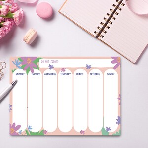 May include: A pink weekly planner with a floral design. The planner has seven columns for each day of the week, Monday through Sunday. The text "Do Not Forget" is at the top of the planner.