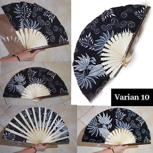 Peut inclure: Un éventail pliant doté d'une toile noire ornée d'un motif floral et tourbillonnant blanc. L'éventail possède des tiges en bois clair et une poignée en bois foncé. Le texte Varian 10 est imprimé en blanc sur un carré noir dans le coin.