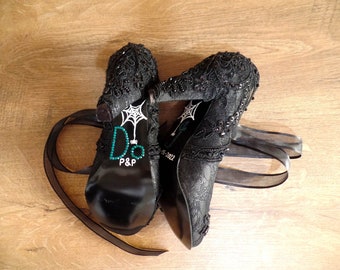 May include: A pair of black lace high heel shoes with a spiderweb and "D&P" written on the heel. The shoes have black ribbon ties.