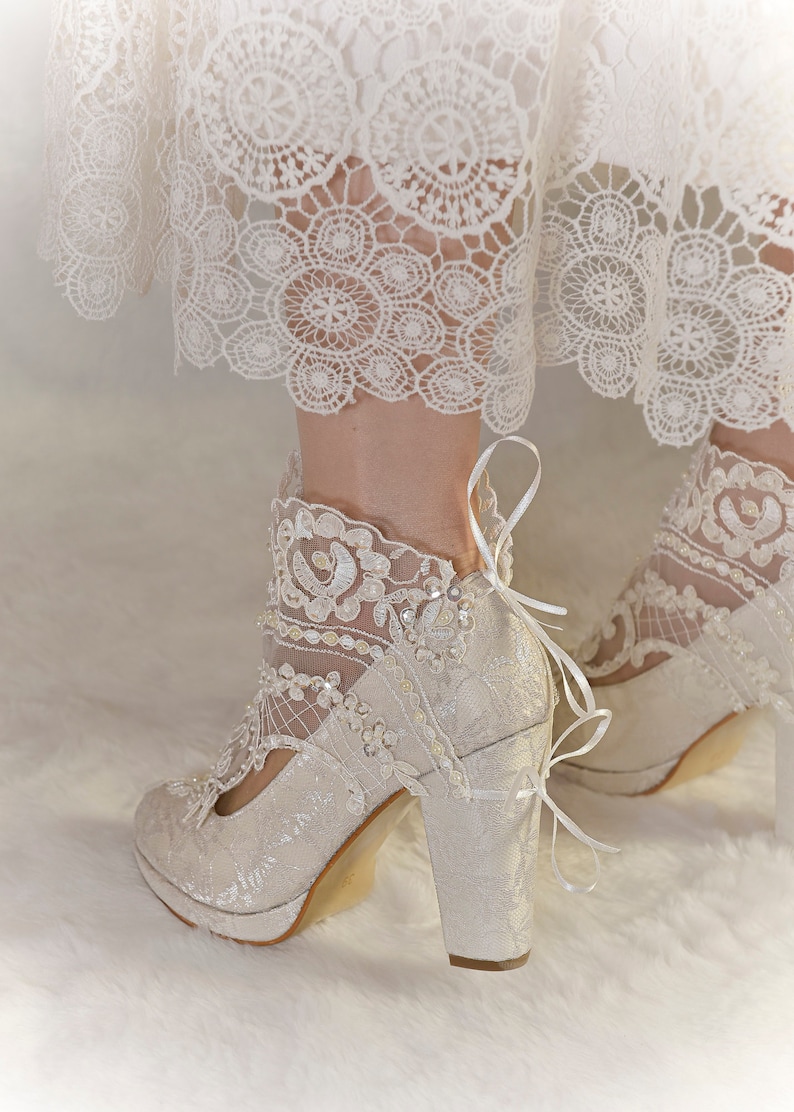 Bride wearing ivory lace wedding boots with pearl and bead embroidery. Floral lace bridal shoes with block heels.