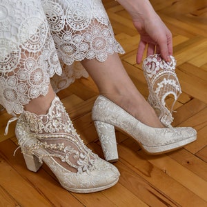 Bride wearing ivory lace wedding boots with pearl and bead embroidery. Floral lace bridal shoes with block heels.