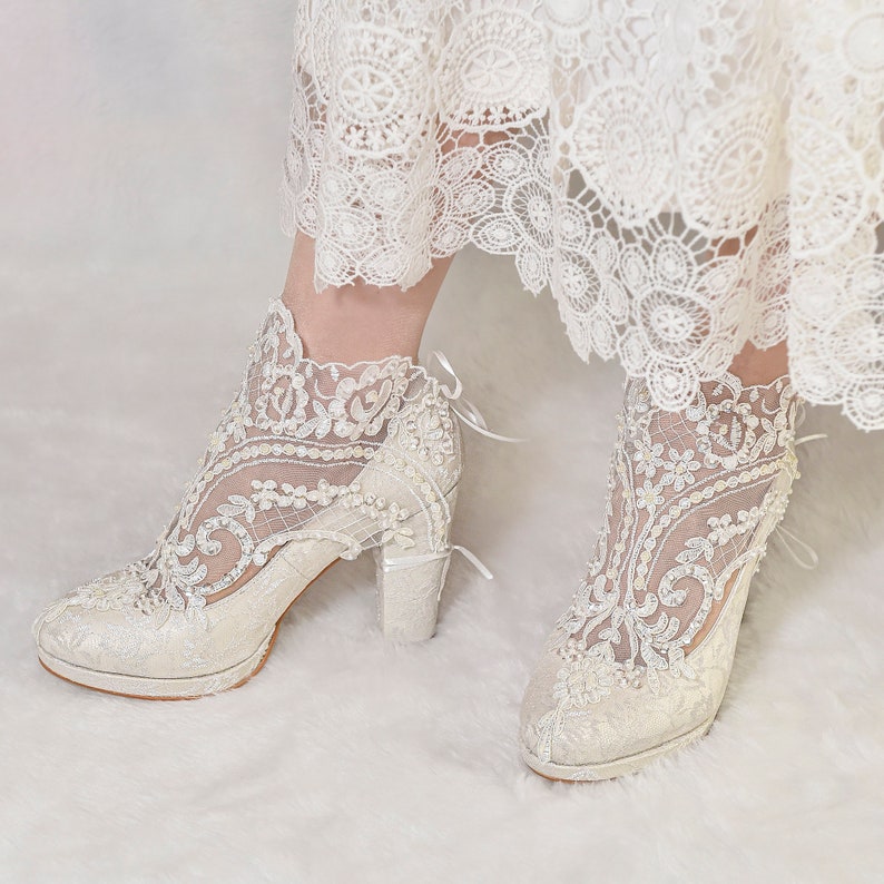 Bride wearing ivory lace wedding boots with pearl and bead embroidery. Floral lace bridal shoes with block heels.