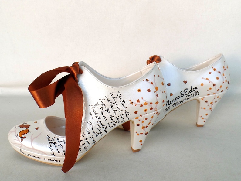 May include: A pair of white satin wedding shoes with a brown ribbon. The shoes are decorated with a floral design and the text "The Book of Love is Long and Boring and Written Very Long Ago. It's Full of Flowers and Heart Shaped Breasts and Things We're All Too Young To Know I Love You" and "Nerea & Eder 1st May 2015".