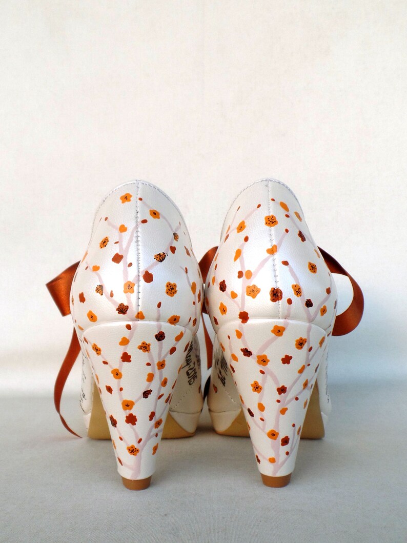 May include: A pair of white satin high-heeled shoes with orange floral designs and orange satin ribbon ties.