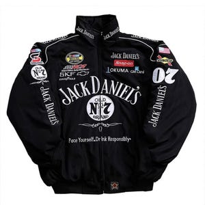 Può includere: Una giacca da corsa nera con zip, caratterizzata dal marchio bianco Jack Daniel's, loghi Old No. 7 e varie toppe di sponsor legati alla NASCAR, tra cui Snap-on, SKF e Goodyear. Il testo 'Pace Yourself. Drink Responsibly.' è stampato sul davanti.