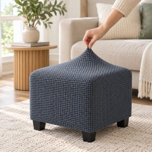 May include: A square ottoman featuring a dark blue, textured, grid-patterned fabric cover. The ottoman is supported by four small, black, block-shaped feet. The fabric has a distinct, raised, waffle-like texture across its entire surface.