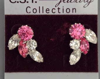 May include: A pair of sparkling earrings from the C.S.T. Jewelry Collection. Each earring features a large, round, hot pink gemstone surrounded by smaller clear and pink stones. The earrings are set against a dark burgundy background.