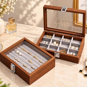 May include: Two rectangular wooden jewelry boxes with clear glass lids and silver metal latches. One box features a gray velvet ring holder insert, while the other contains multiple square compartments lined with gray velvet for storing various earrings and small accessories.