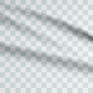Könnte beinhalten: Ein Textilstoff mit einem sich wiederholenden Karomuster aus abwechselnden hellen salbeigrünen und weißen Quadraten. Das Material weist weiche, diagonale Falten auf der Oberfläche auf, die die Textur und das gleichmäßige Gitterdesign betonen.
