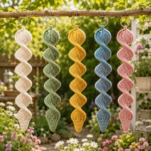May include: Five spiral-shaped crochet ornaments hanging from a wooden branch. Each ornament features a distinct solid color: cream, sage green, mustard yellow, dusty blue, and soft pink. Each piece is attached to a silver metal ring at the top.