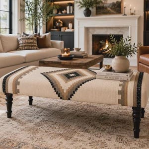May include: A rectangular ottoman featuring a cream-colored fabric with a central diamond pattern in shades of brown, tan, and black. The piece is supported by four dark brown, turned wooden legs and displays a woven texture across the top surface.