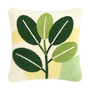 May include: A square throw pillow with a tufted texture featuring a central plant motif with dark green and light green leaves. The background consists of an off-white base with abstract patches of pale yellow and soft green color blocks.