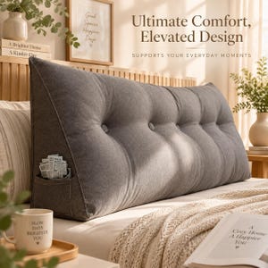 Puede incluir: Una almohada de cama grande en forma de cuña de color gris carbón con un diseño capitoné, botones forrados de tela y un pequeño bolsillo lateral. La almohada está sobre una cama con ropa blanca, junto a una taza blanca y un libro abierto.