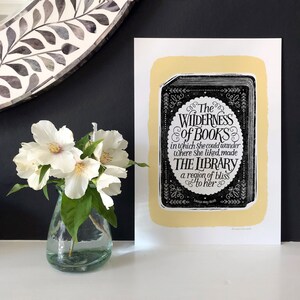 May include: A black and white print with a yellow background featuring a quote about books and libraries. The quote reads "The Wilderness of Books in which she could wander where she liked, made The Library a region of bliss to her." The quote is attributed to "Louisa May Alcott".