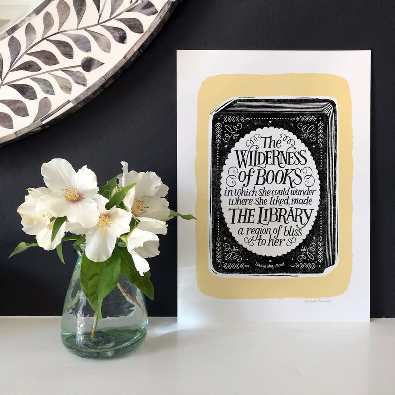 May include: A black and white print with a yellow background featuring a quote about books and libraries. The quote reads "The Wilderness of Books in which she could wander where she liked, made The Library a region of bliss to her." The quote is attributed to "Louisa May Alcott".
