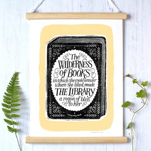 May include: Black and white print with a yellow background featuring a quote about books and libraries by Louisa May Alcott. The quote reads "The Wilderness of Books in which she could wander where she liked, made The Library a region of bliss to her."