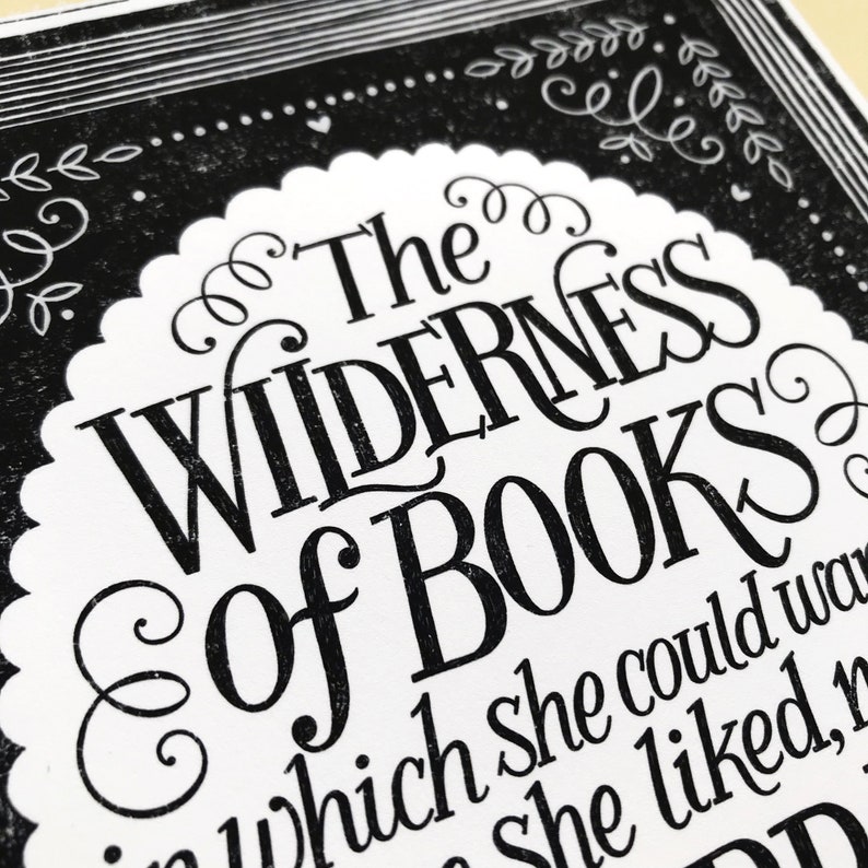 May include: Black and white typography print with the text "The Wilderness of Books" in a decorative font. The text is surrounded by a decorative border of swirls and leaves.