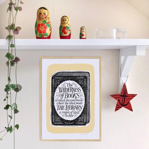 May include: A framed print with a yellow background and a black and white illustration of a book with the text "The Wilderness of Books in which she could wander where she liked, made THE LIBRARY a region of bliss to her".
