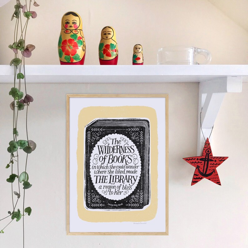 May include: A framed print with a yellow background and a black and white illustration of a book with the text "The Wilderness of Books in which she could wander where she liked, made THE LIBRARY a region of bliss to her".
