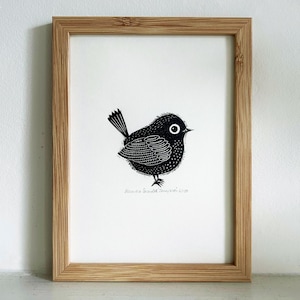 May include: A framed print with a black and white illustration of a round bird with a detailed wing pattern and a small tail. The bird has a large eye and is set against a white background. The frame is made of light brown wood.