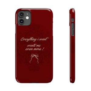 Peut inclure: Une coque de smartphone rouge foncé avec un motif floral subtil et sombre en arrière-plan. Le texte "Everything i want wants me even more !" est imprimé dans une police cursive beige clair au-dessus d'une illustration au trait d'un nœud.