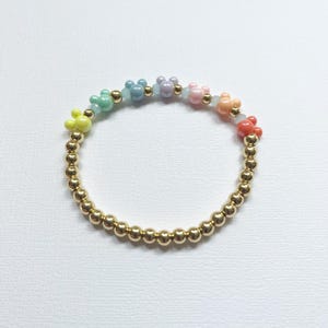May include: A beaded bracelet featuring a rainbow of pastel-colored Mickey Mouse-shaped beads interspersed with gold-colored beads. The bracelet is made of small, round, gold-colored beads.