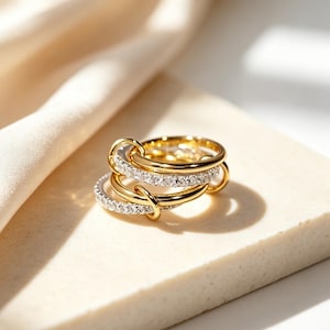Könnte beinhalten: Ein mehrreihiger Ring mit ineinandergreifenden goldfarbenen Metallbändern und Bändern, die mit kleinen, klaren, funkelnden Steinen besetzt sind. Das Design besteht aus mehreren dünnen, kreisförmigen Ringen, die zu einem Schmuckstück verbunden sind.