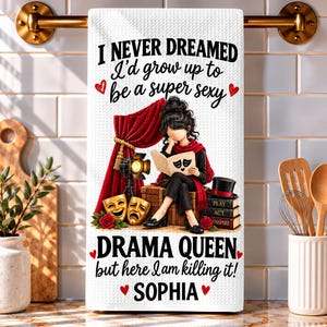 May include: A white waffle-textured kitchen towel featuring a graphic of a person sitting on a trunk with theater masks, red curtains, and books. The text reads: I NEVER DREAMED I'd grow up to be a super sexy DRAMA QUEEN but here I am killing it! SOPHIA.