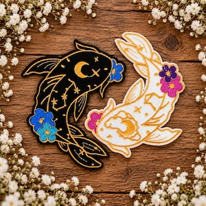 May include: Two embroidered koi fish patches, one black with gold celestial patterns and blue flowers, the other white with gold celestial patterns and purple and pink flowers. The patches are arranged in a curved, yin-yang style formation.
