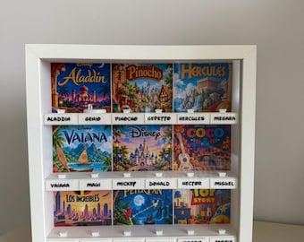 Könnte beinhalten: Ein weißes Vitrinenregal mit drei Ebenen und neun quadratischen Disney-Filmbildern. Unter jedem Bild befinden sich zwei beschriftete Fächer mit Namen wie Aladdin, Genio, Pinocho, Gepetto, Hercules, Megara, Vaiana, Maui, Mickey, Donald, Hector, Miguel, Mr. Increible, Elastigirl, Peter Pan, Campanilla, Woody und Jessie.