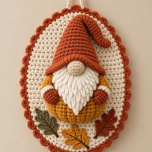 May include: An oval crochet wall hanging featuring a gnome with a tall orange hat, a white beard, and a mustard yellow body. The gnome sits on a cream-colored background with three crocheted leaves in green, yellow, and rust orange at the base.
