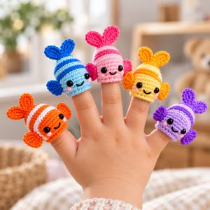 May include: A set of five colorful crocheted fish finger puppets in blue, pink, yellow, orange, and purple. Each small fish features a striped pattern, a smiling face with black eyes, and two side fins, designed to fit onto individual fingers.