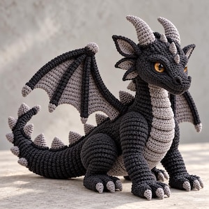 May include: A crocheted dragon figurine featuring a dark charcoal body with light gray accents on the underbelly, wings, horns, and tail spikes. The creature has large, amber-colored eyes and a textured, stitched surface throughout its entire form.
