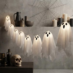 Peut inclure: Une guirlande lumineuse LED composée de fantômes blancs en tissu translucide avec des yeux et des bouches noirs imprimés. Chaque fantôme s'illumine de l'intérieur. La guirlande est suspendue horizontalement pour un effet décoratif.