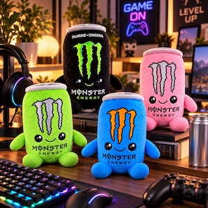 May include: Four plush toys shaped like energy drink cans in black, pink, lime green, and blue. Each plush features the Monster Energy logo, a smiling face with large black eyes, small arms, and feet. The text "TAURINE+GINSENG" is on the black can.
