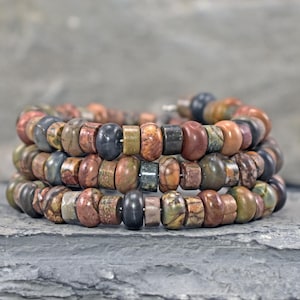 May include: A multi-strand wrap bracelet composed of small, round, earth-toned stone beads in shades of brown, gray, green, and tan. The beads feature varied natural textures and patterns, arranged in a continuous circular coil design.