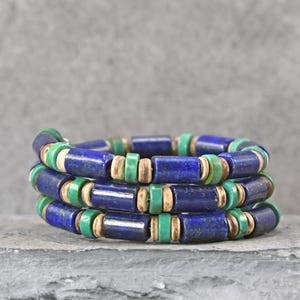 May include: A multi-strand wrap bracelet featuring cylindrical deep blue beads, small round green beads, and thin tan spacers. The bracelet is constructed with a repeating pattern of these three bead types, creating a layered, circular design.