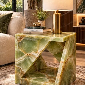May include: A square side table crafted from green onyx stone with a geometric cutout design. The table features natural veining in shades of light green, dark green, and white, with a polished finish and a hollow center section.