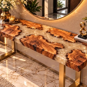 May include: A rectangular console table featuring a live-edge wood slab surface embedded in translucent white resin. The table is supported by a gold-toned metal frame with U-shaped legs. A circular logo with a crown and the text RoyalStoneMade is visible.