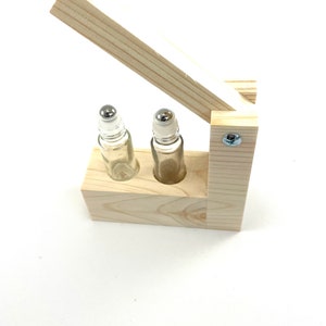 May include: A wooden box with a hinged lid, designed to hold two small glass roller bottles with metal roller balls. The box is made of light-colored wood and has a natural finish.