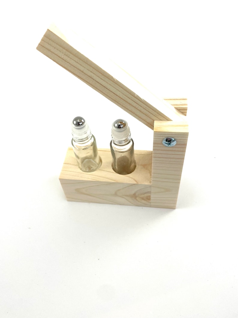 May include: A wooden box with a hinged lid, designed to hold two small glass roller bottles with metal roller balls. The box is made of light-colored wood and has a natural finish.