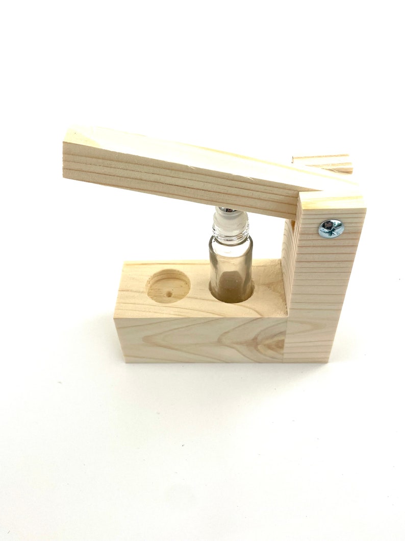 May include: A wooden bottle stopper with a clear glass bottle inside. The stopper is made of light wood and has a simple design. The bottle is held in place by a wooden frame.