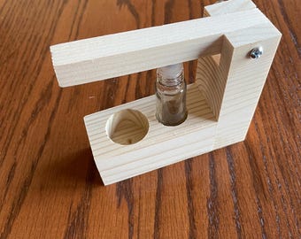 May include: A wooden roller bottle holder with a small glass bottle inside. The holder is made of light wood and has a simple design.