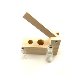 May include: A wooden roller bottle holder with two empty glass roller bottles. The holder has two slots for the bottles and a hinged lid.