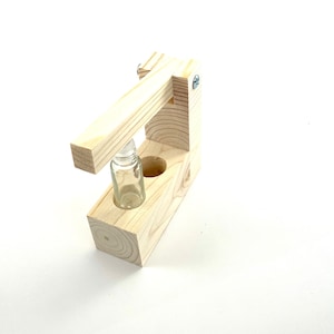 May include: A wooden bottle holder with a lever to press down on the bottle. The holder has a clear glass bottle inside.