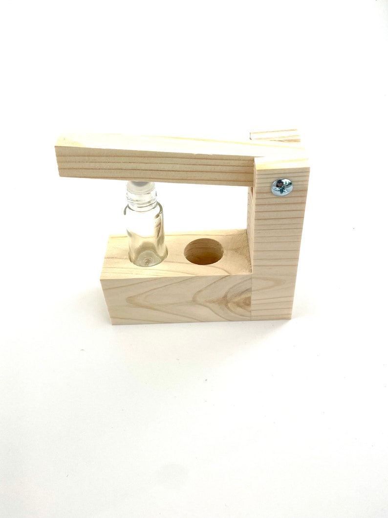 May include: A wooden stand with a small glass bottle in the center. The stand has a hinged top that can be lifted to access the bottle.